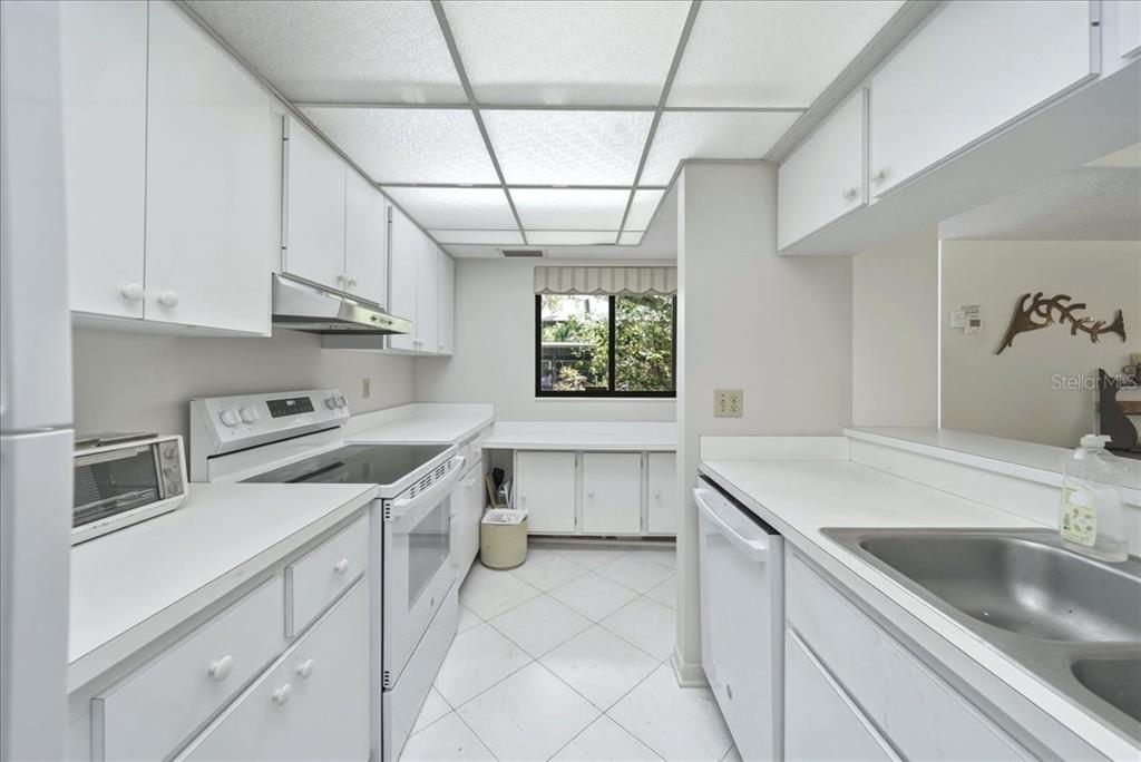 A white galley kitchen features tile flooring, laminate countertops, and a drop ceiling — 1711 PELICAN COVE ROAD UNIT 341, SARASOTA, FL