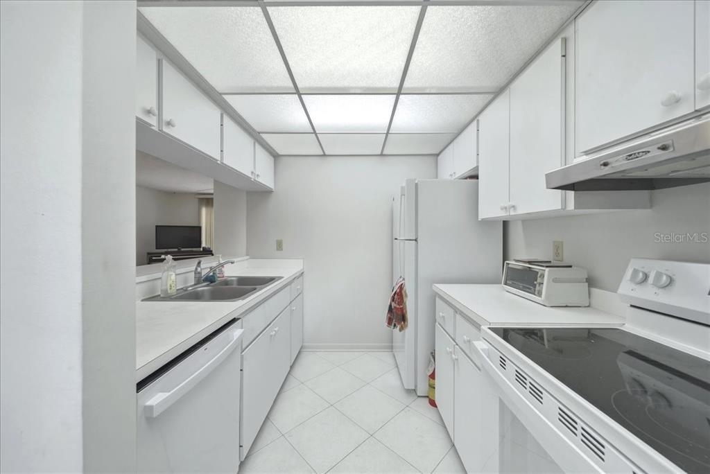 A galley-style kitchen features white cabinets, white appliances, and a drop ceiling with fluorescent lighting — 1711 PELICAN COVE ROAD UNIT 341, SARASOTA, FL