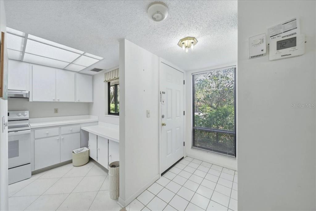 A kitchen with white cabinets and tile flooring sits adjacent to an entryway with a door — 1711 PELICAN COVE ROAD UNIT 341, SARASOTA, FL