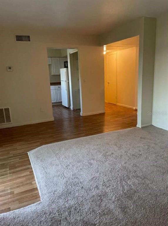 A living room with carpet and wood-look flooring leads to a kitchen and hallway — 5885 DAHLIA DRIVE UNIT 30/215, ORLANDO, FL