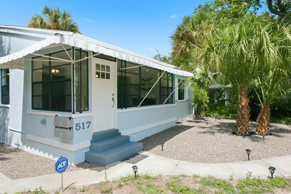 A light blue house features a screened-in front porch, white trim, and a gravel yard — 517 41ST AVENUE S, ST PETERSBURG, FL
