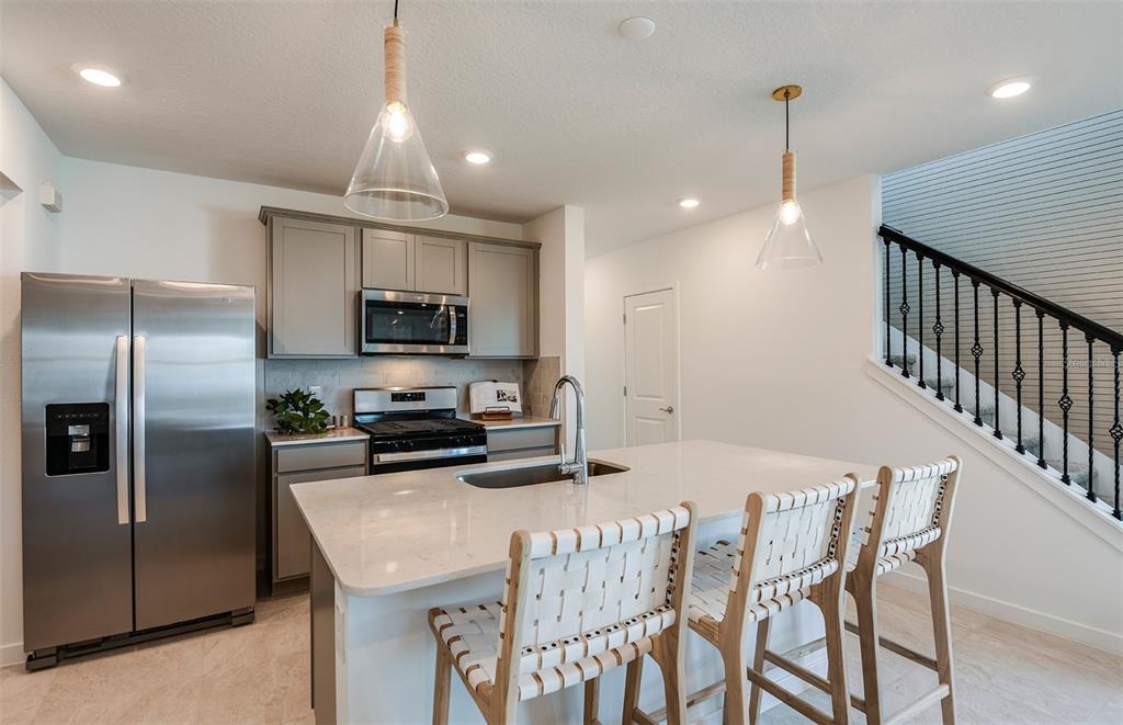 A kitchen features stainless steel appliances, gray cabinets, a quartz island, and woven bar stools — 1444 HAMILTON WAY, LAKE ALFRED, FL