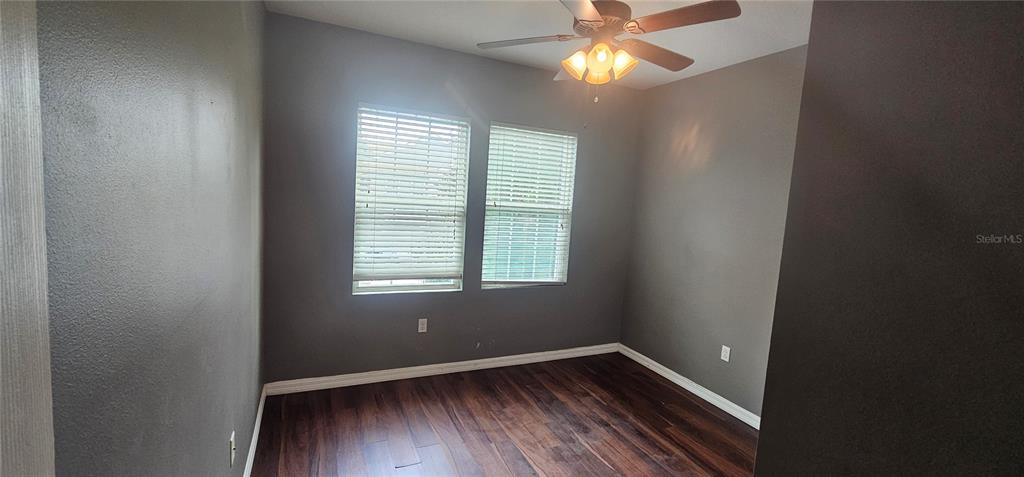An empty room features dark gray walls, wood-look flooring, two windows with blinds, and a ceiling fan — 9313 SHEPTON STREET, ORLANDO, FL