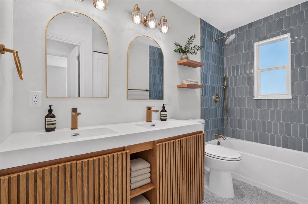 A bathroom features a double vanity with wood-slatted cabinets, arched mirrors, and blue tile walls — 2960 EMERSON AVENUE S, ST PETERSBURG, FL