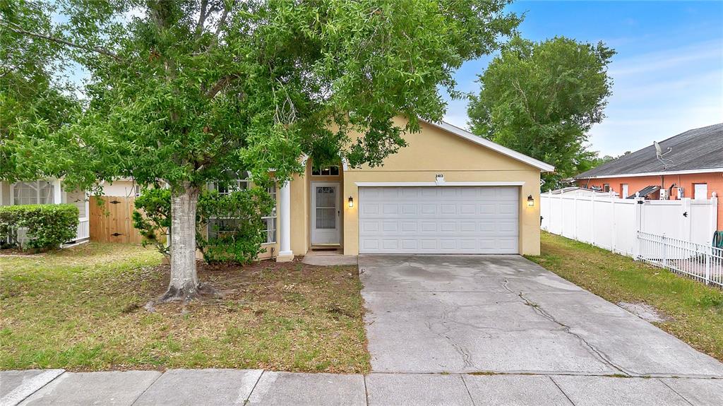A single-story house with a beige stucco exterior, a two-car garage, and a front tree — 2413 RADNOR AVENUE, ORLANDO, FL