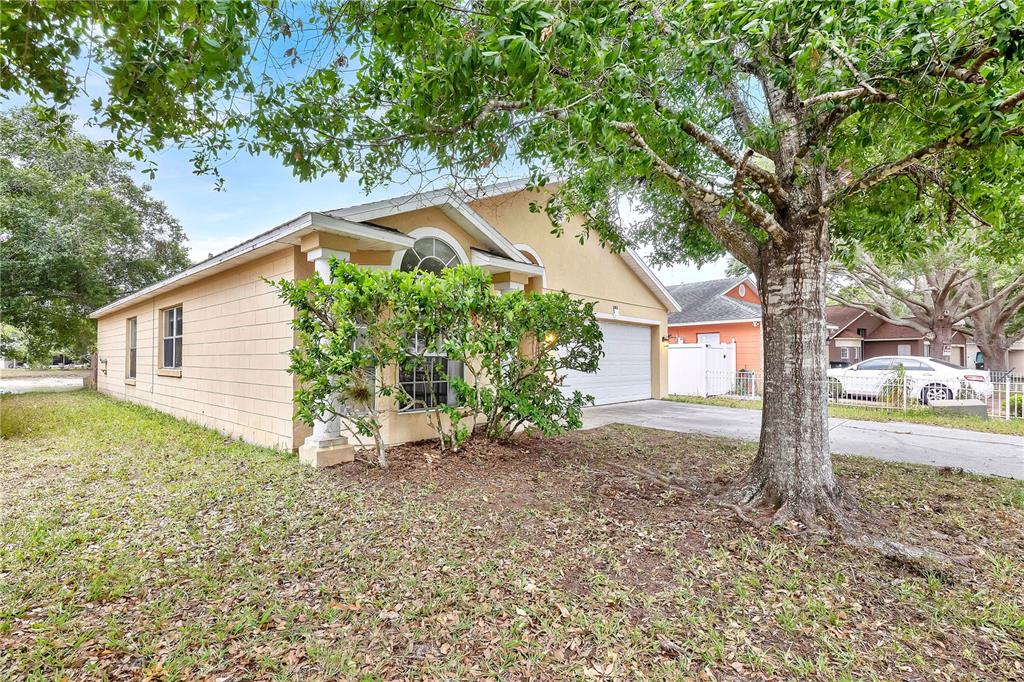 A single-story house with a tan exterior, a two-car garage, and a large front tree — 2413 RADNOR AVENUE, ORLANDO, FL