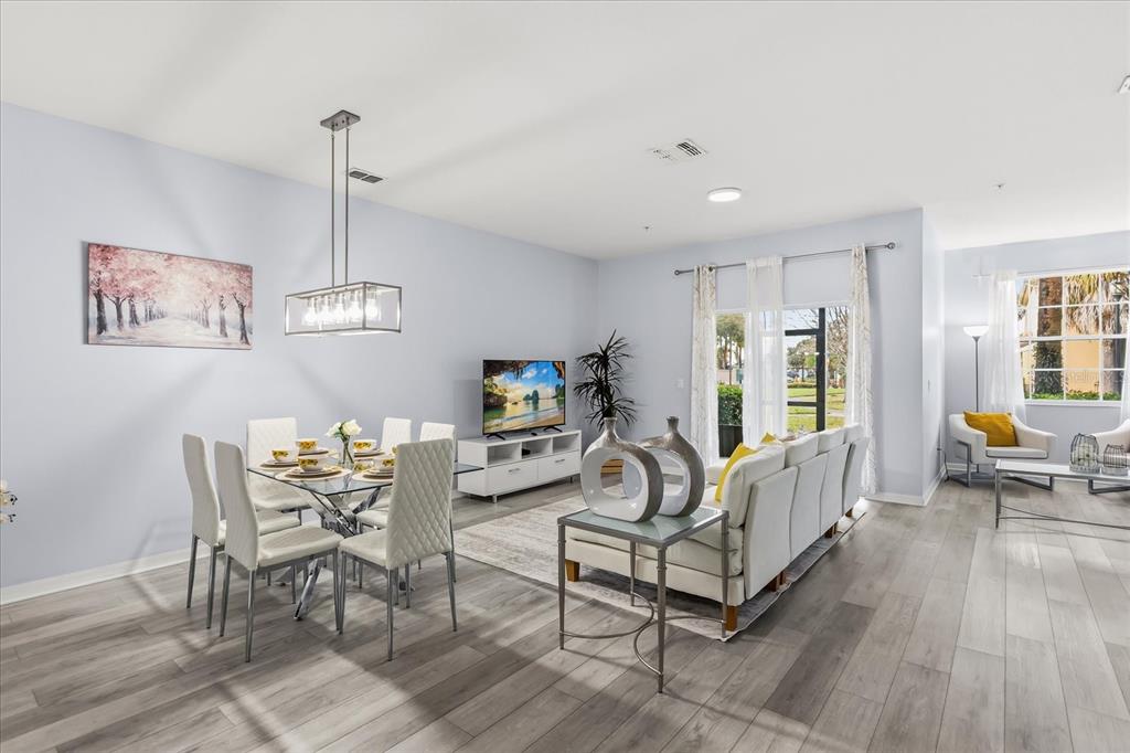 An open-concept living and dining area features light gray walls, wood-look flooring, and modern furniture — 7525 BLISS WAY, KISSIMMEE, FL