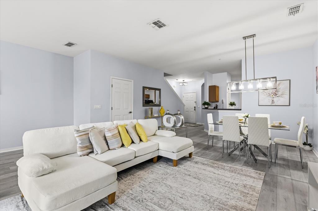 A living and dining area features a white sectional sofa, a glass dining table, and light-colored flooring — 7525 BLISS WAY, KISSIMMEE, FL