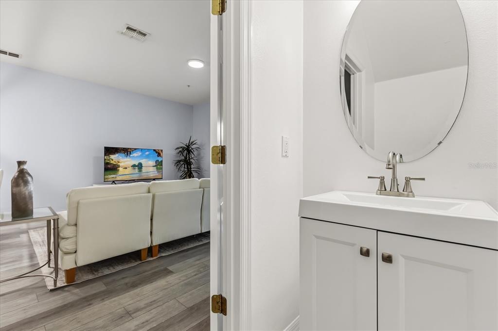 A white bathroom vanity with an oval mirror overlooks a living room with a sofa — 7525 BLISS WAY, KISSIMMEE, FL
