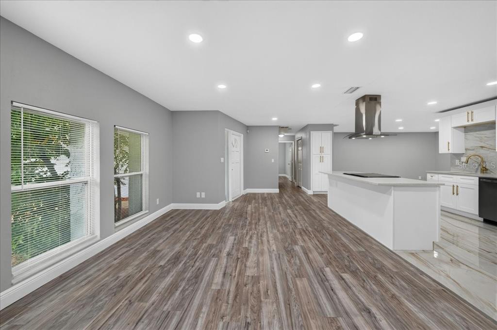 A bright open-concept room features wood-look flooring, recessed lighting, and a modern white kitchen island — 2964 MEADOW OAK DRIVE S, CLEARWATER, FL