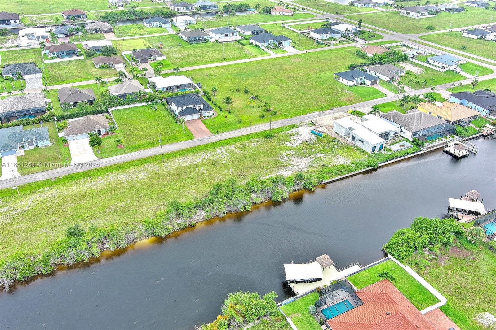 An aerial view shows a residential neighborhood with houses, vacant lots, and a canal — 1228 NW 34th Ave, Cape Coral FL 33993, CAPE CORAL, FL