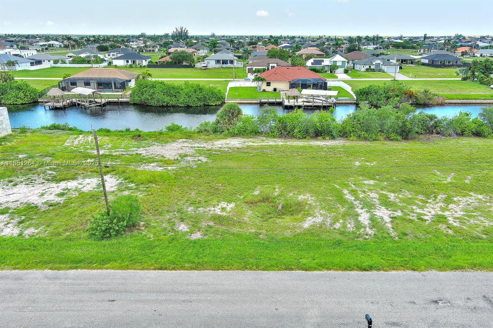 An aerial view shows a vacant grassy lot fronting a canal with neighboring houses nearby — 1228 NW 34th Ave, Cape Coral FL 33993, CAPE CORAL, FL