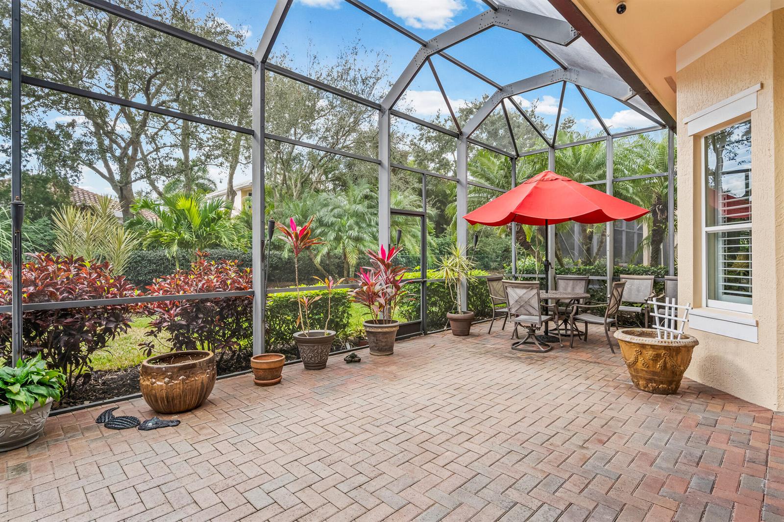 A screened-in patio features brick pavers, potted plants, and a dining set with a red umbrella — 1209 River Wind Circle, Vero Beach FL 32967, VERO BEACH, FL