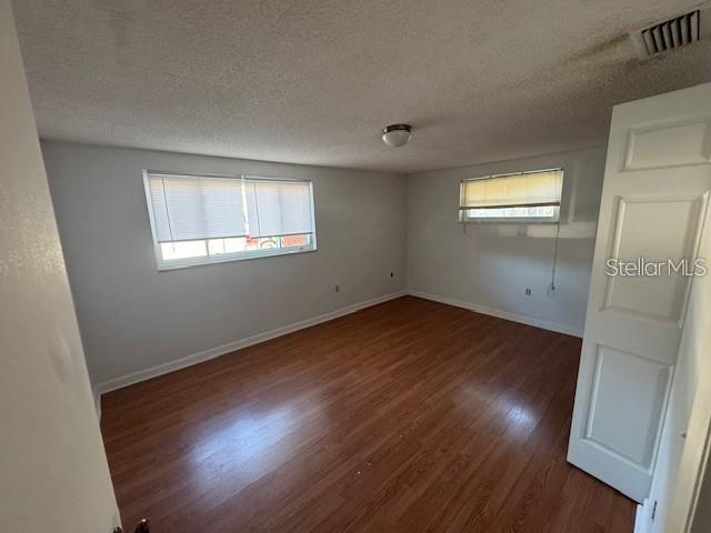 An empty room features light gray walls, wood-look flooring, and two windows with blinds — 7235 REDBUD COURT, NEW PORT RICHEY, FL
