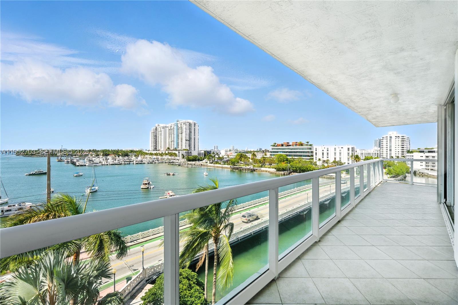 A balcony with white tile flooring overlooks a bay, a marina, and a bridge — 10 Venetian Way # 604, Miami Beach FL 33139, MIAMI BEACH, FL