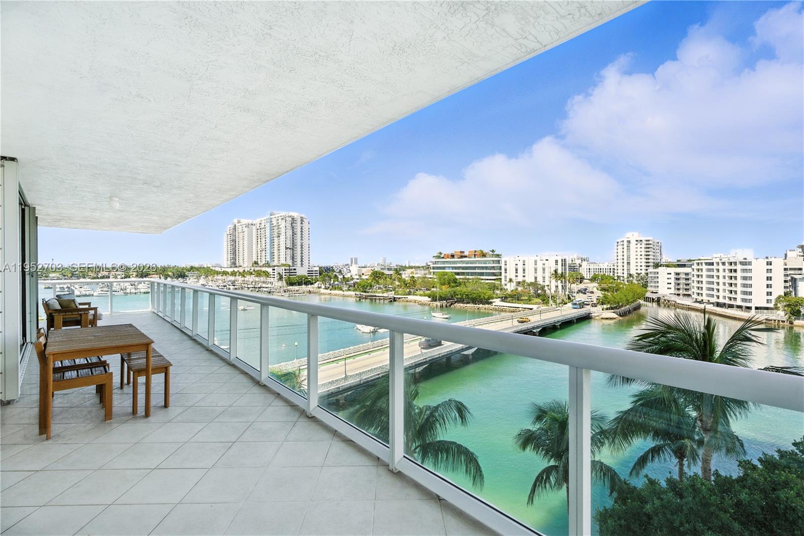 A balcony with a wooden table and chairs overlooks a bridge, water, and city buildings — 10 Venetian Way # 604, Miami Beach FL 33139, MIAMI BEACH, FL