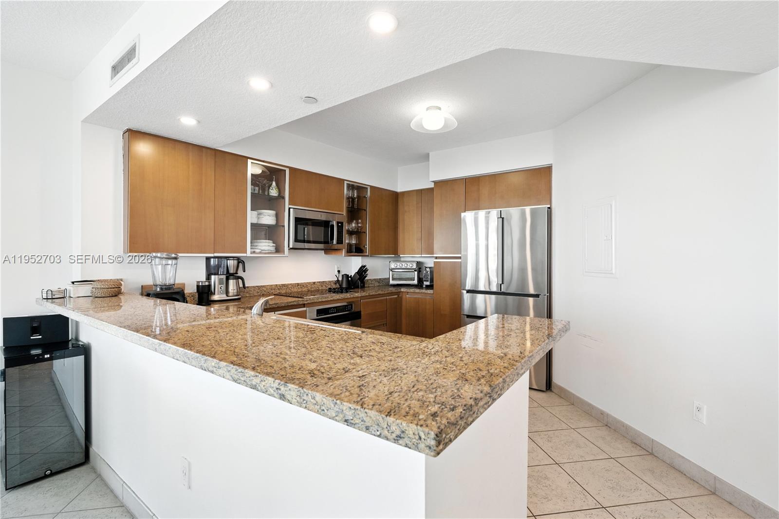 A kitchen features wood cabinets, granite countertops, stainless steel appliances, and tile flooring — 10 Venetian Way # 604, Miami Beach FL 33139, MIAMI BEACH, FL