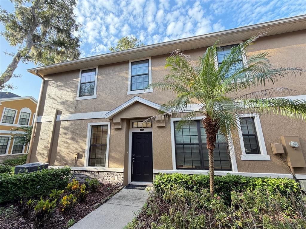 A two-story tan stucco townhouse features a black front door and a small palm tree — 5722 KINGLETHILL DRIVE, LITHIA, FL
