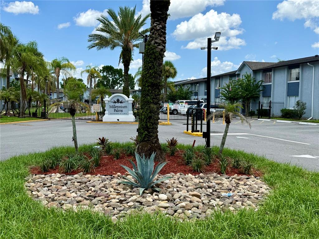 A landscaped island with a palm tree and sign marks the entrance to Millennium Palms — 4805 S TEXAS AVENUE UNIT 4805C, ORLANDO, FL