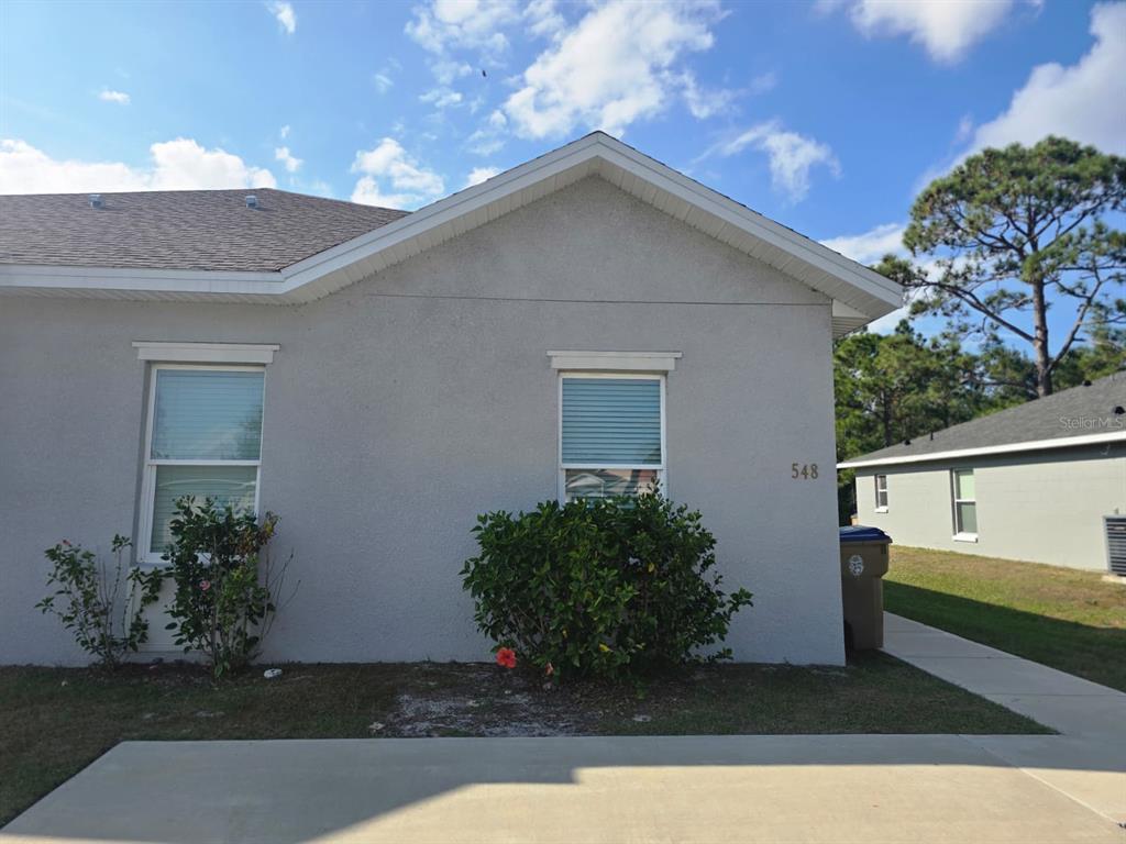 A single-story house exterior features a light gray stucco facade with two windows and landscaping — 546 IMPERIAL PL UNIT 548, KISSIMMEE, FL