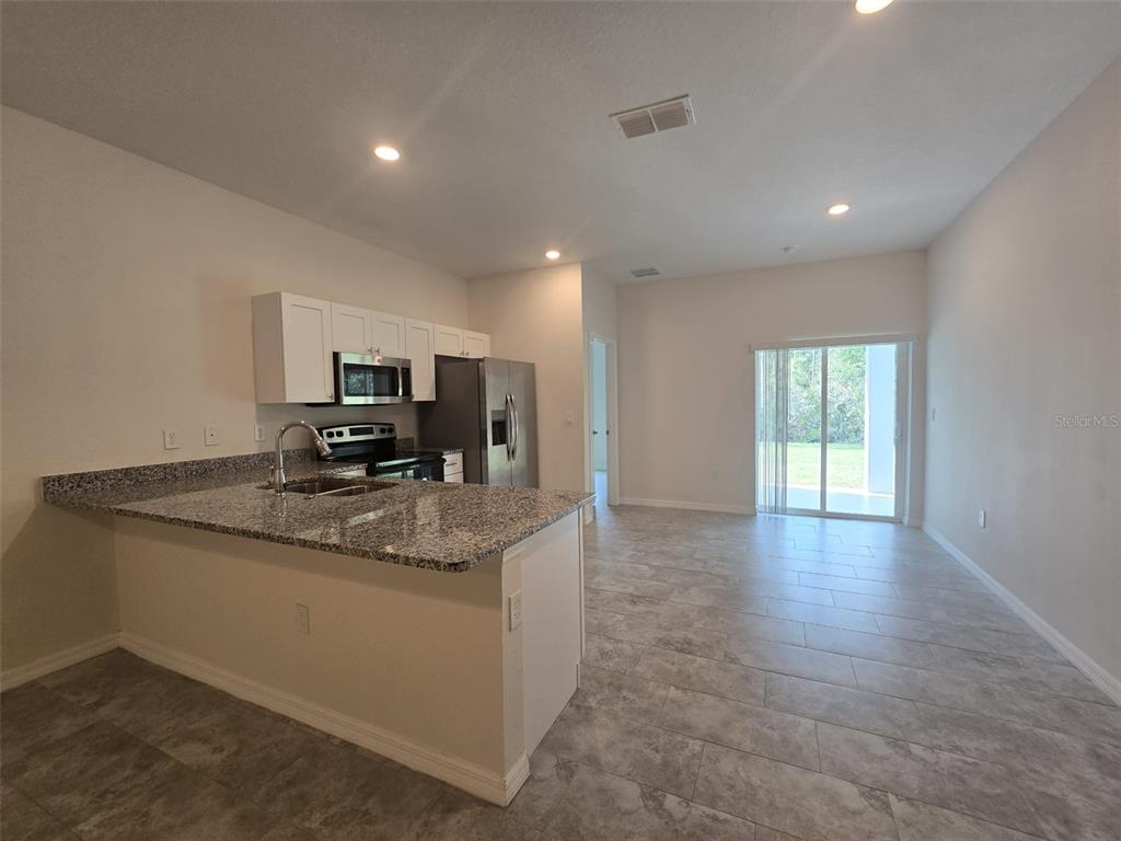 A kitchen with granite countertops and stainless steel appliances opens to a tiled living area — 546 IMPERIAL PL UNIT 548, KISSIMMEE, FL