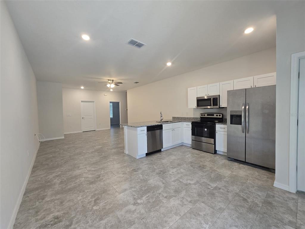 An open-concept kitchen features white cabinets, stainless steel appliances, and gray tile flooring — 546 IMPERIAL PL UNIT 548, KISSIMMEE, FL