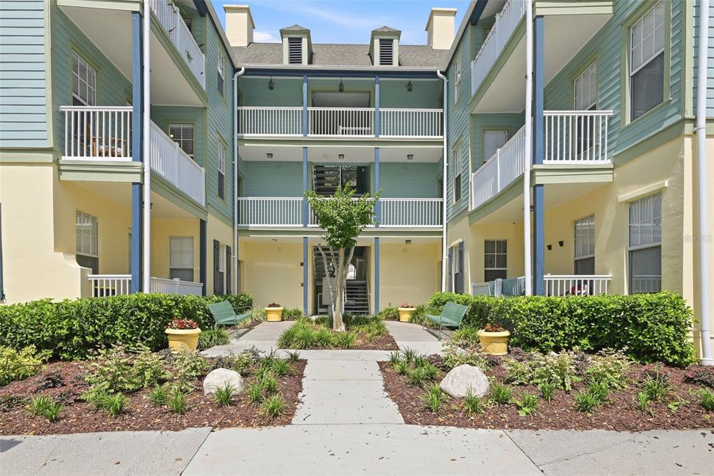 A three-story apartment building exterior features light green siding, white railings, and a central walkway — 611 CAMPUS STREET UNIT 280, CELEBRATION, FL