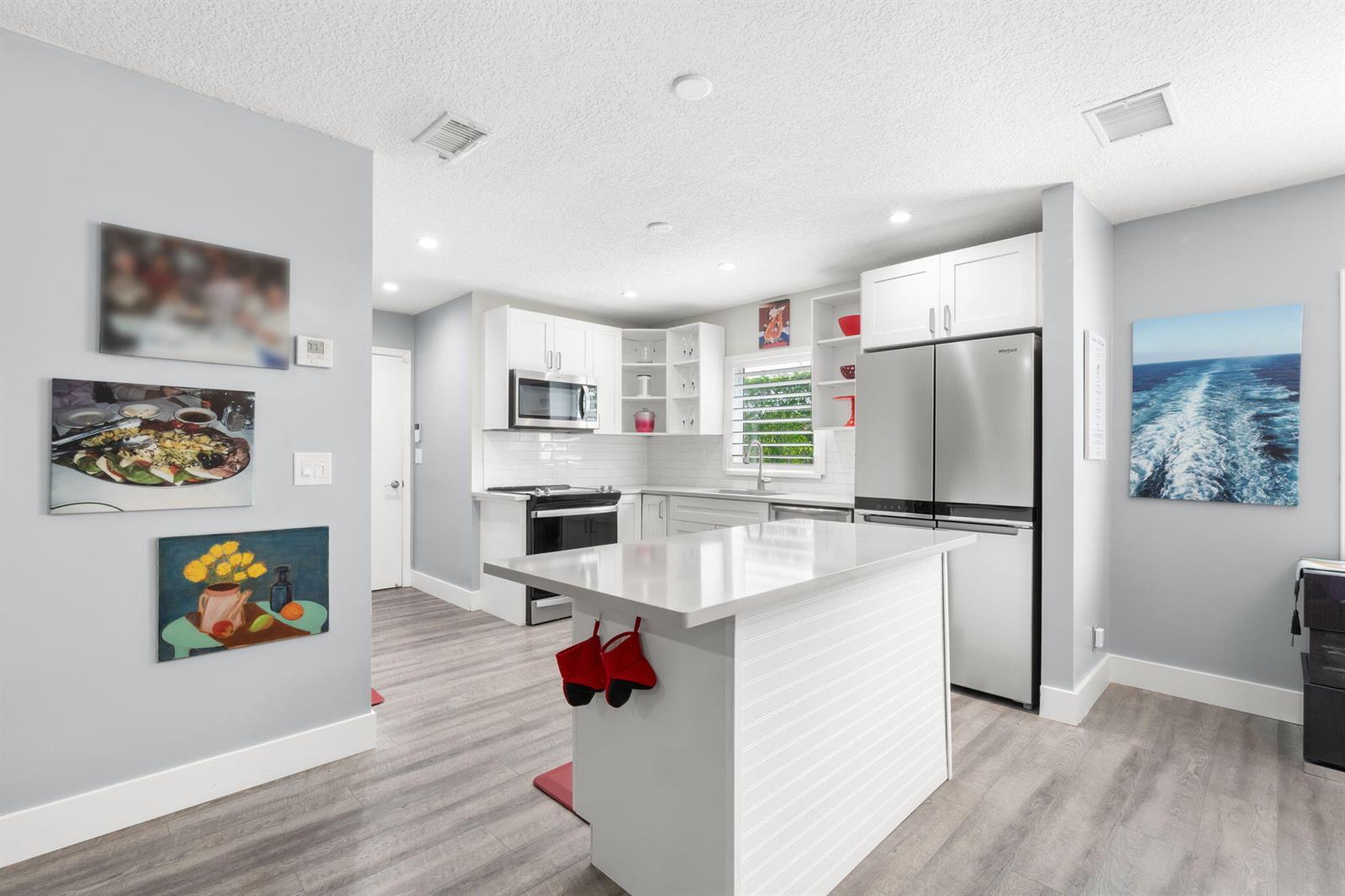 A modern kitchen features white cabinetry, stainless steel appliances, a center island, and gray flooring — 13491 Via Vesta, Delray Beach FL 33484, DELRAY BEACH, FL