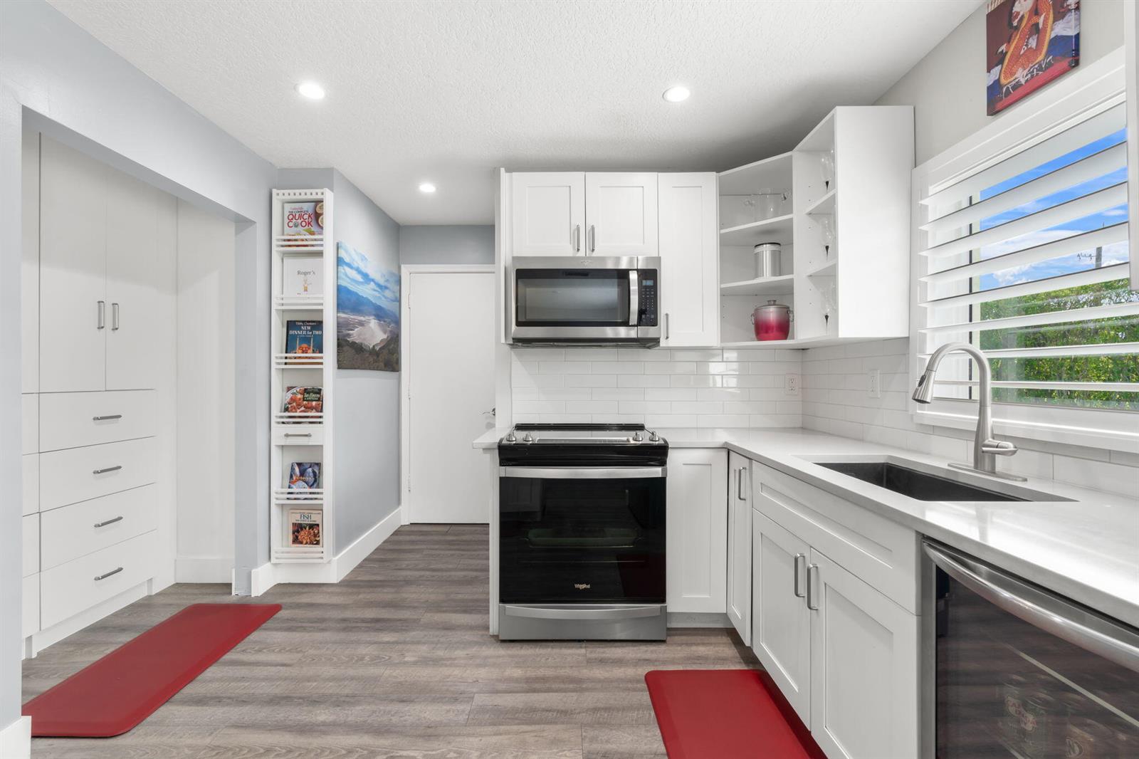 A modern kitchen features white cabinetry, stainless steel appliances, subway tile backsplash, and wood-look flooring — 13491 Via Vesta, Delray Beach FL 33484, DELRAY BEACH, FL