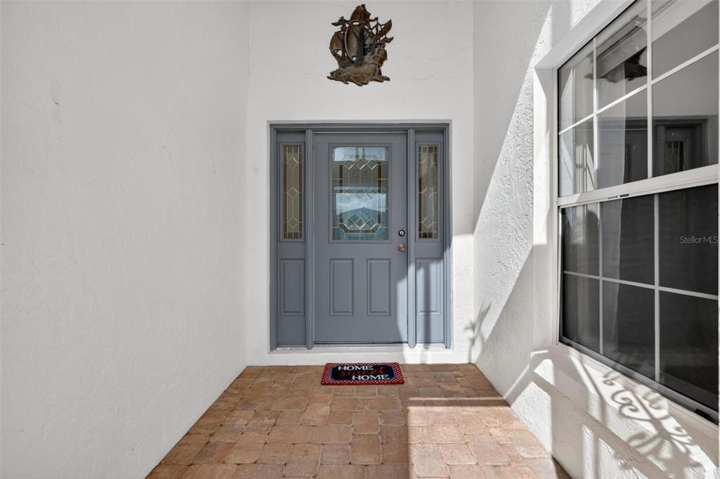 A gray front door with sidelights and a ship wall hanging on a covered porch — 17808 SE 115TH COURT, SUMMERFIELD, FL