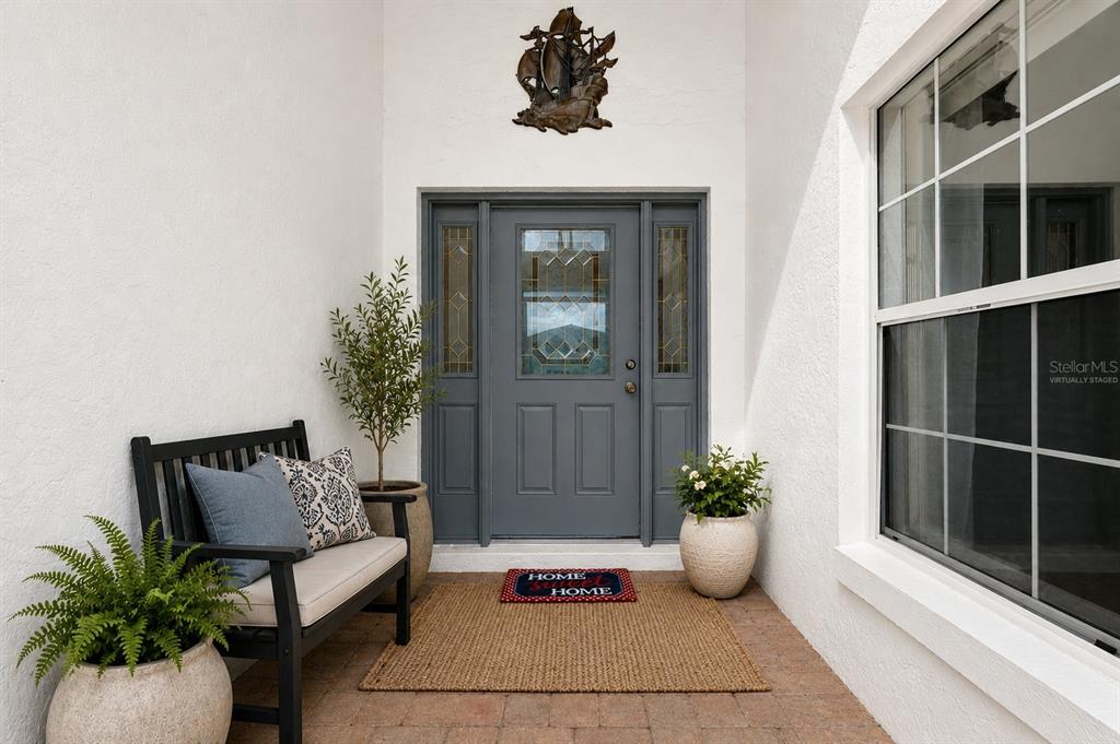 A front entryway features a gray door, a black bench, potted plants, and a rug — 17808 SE 115TH COURT, SUMMERFIELD, FL