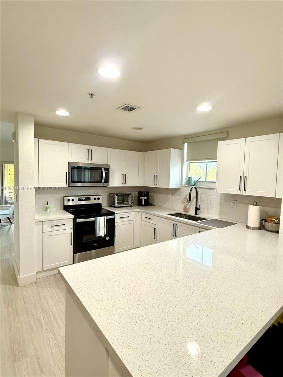 A kitchen features white cabinets, light countertops, a stainless steel oven, and a peninsula — 8999 NW 107th Ct # 1, Doral FL 33178, DORAL, FL