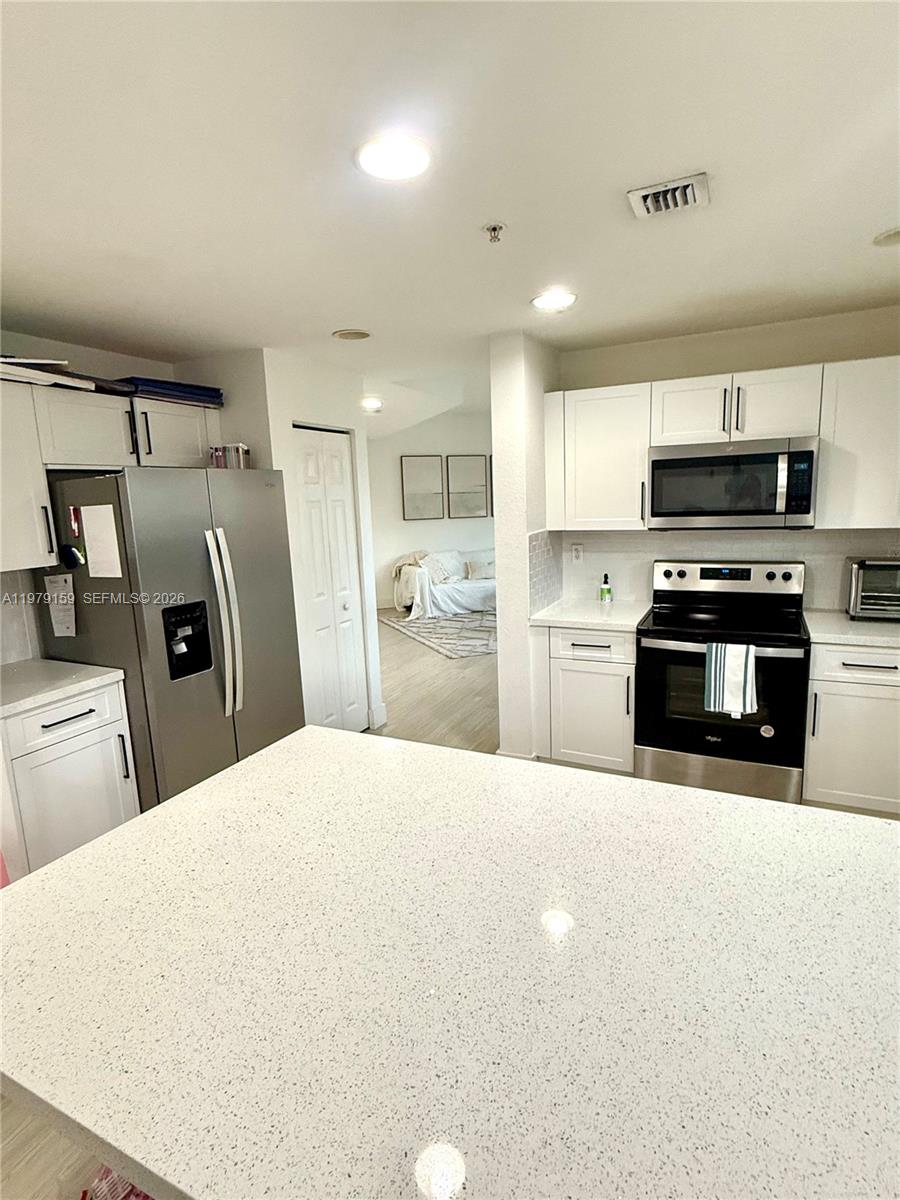 A kitchen features white cabinets, stainless steel appliances, and a large speckled quartz island — 8999 NW 107th Ct # 1, Doral FL 33178, DORAL, FL