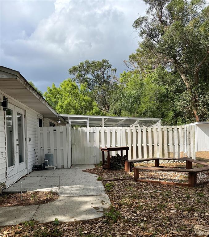 A backyard features a concrete patio, a white fence, a wooden table, and surrounding trees — 2419 WELLS AVENUE, SARASOTA, FL