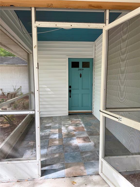 A screened-in porch features a tiled floor and a teal front door with house numbers — 2419 WELLS AVENUE, SARASOTA, FL
