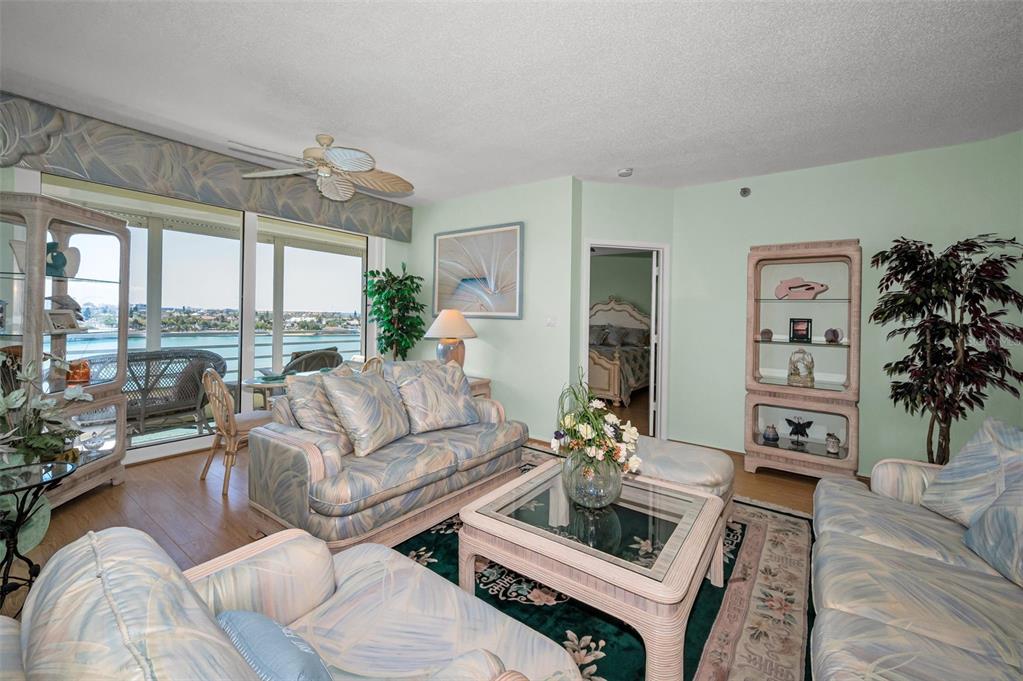 A living room features floral-patterned furniture, a glass-top coffee table, and a view of water — 7882 SAILBOAT KEY BOULEVARD S UNIT 605, SOUTH PASADENA, FL