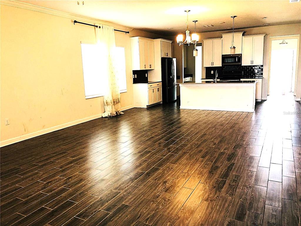 An open-concept kitchen and living area features dark wood-look tile flooring and white cabinetry — 4625 RHYTHM ROAD, KISSIMMEE, FL