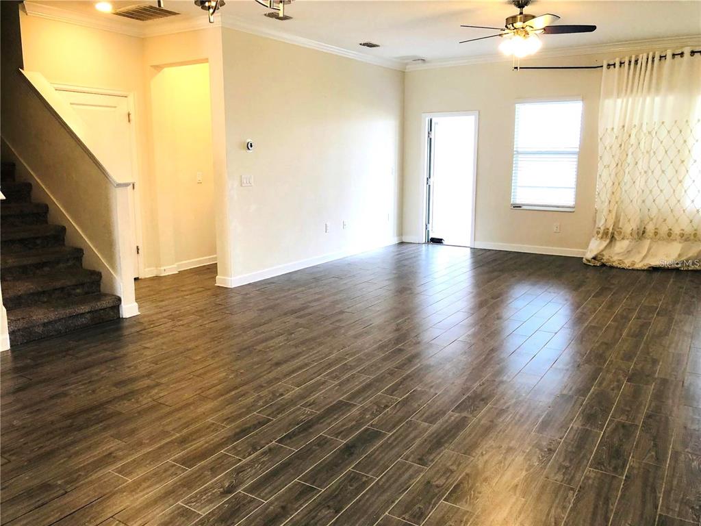 An open living room features wood-look tile flooring, a staircase, and a ceiling fan — 4625 RHYTHM ROAD, KISSIMMEE, FL