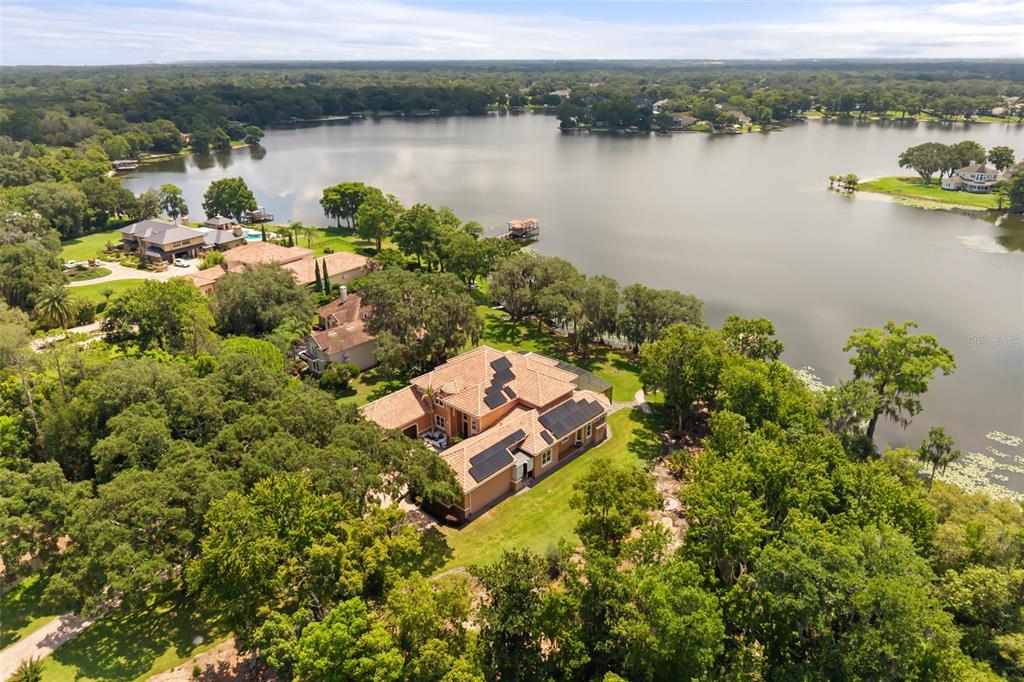 An aerial view shows a large house with solar panels on a tile roof near a lake — 2117 STURBRIDGE COURT, WINTER SPRINGS, FL