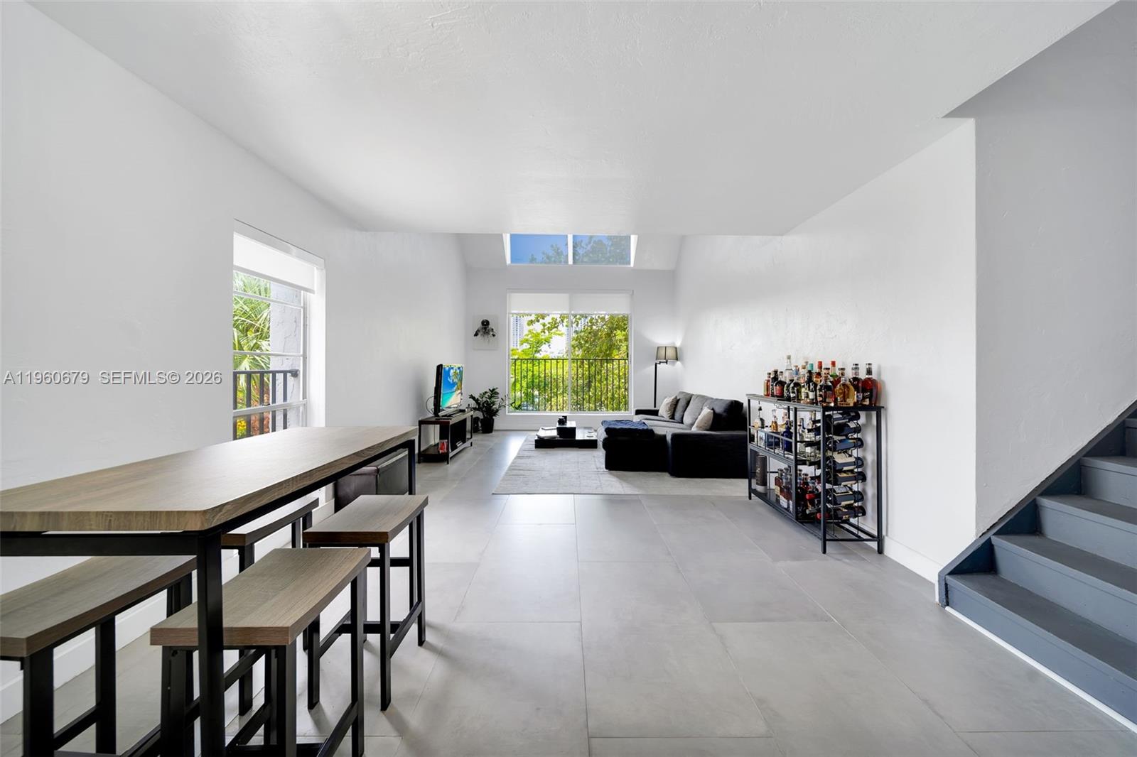 A modern living room features gray tile floors, a dining area, and a balcony view — 6900 N Kendall Dr # A303, Pinecrest FL 33156, PINECREST, FL