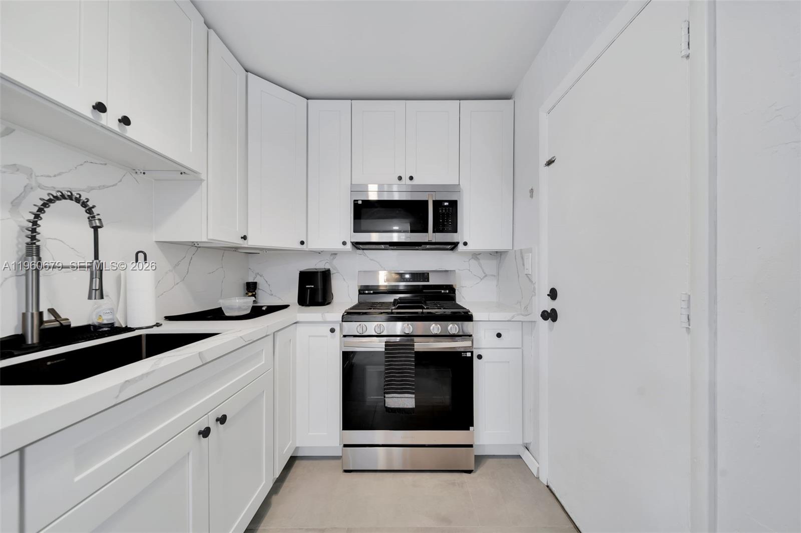 A compact kitchen features white cabinets, stainless steel appliances, and a black sink — 6900 N Kendall Dr # A303, Pinecrest FL 33156, PINECREST, FL