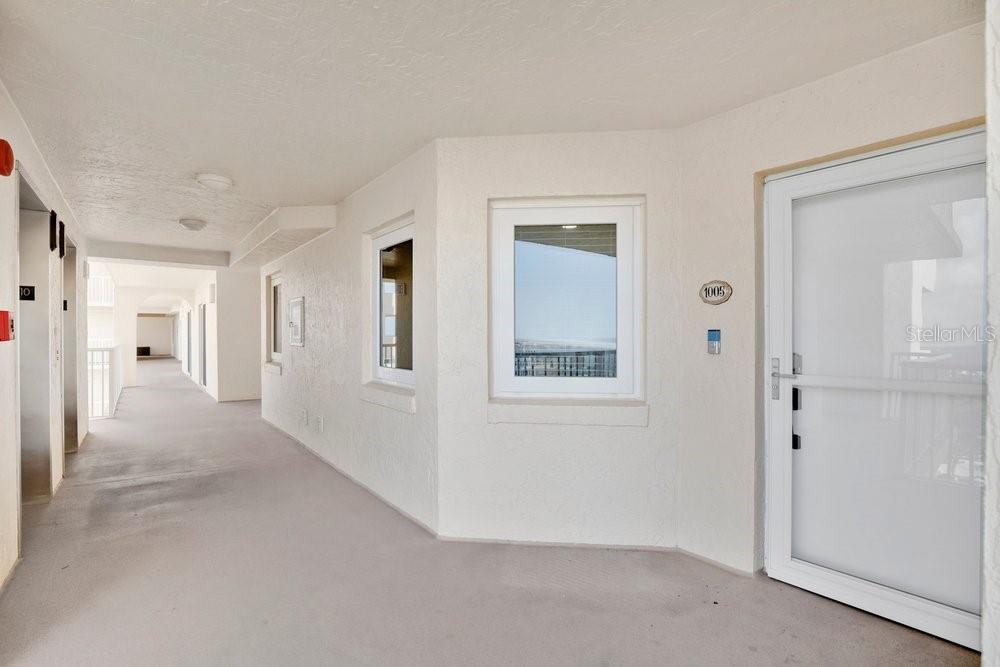 An outdoor apartment hallway features a white door labeled 1005 and several windows — 257 MINORCA BEACH WAY UNIT 1005, NEW SMYRNA BEACH, FL