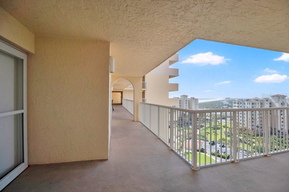 A covered balcony with a white railing overlooks a coastal landscape and nearby buildings — 257 MINORCA BEACH WAY UNIT 1005, NEW SMYRNA BEACH, FL