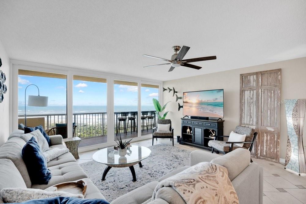 A living room with a gray sofa, glass coffee table, and a balcony overlooking the ocean — 257 MINORCA BEACH WAY UNIT 1005, NEW SMYRNA BEACH, FL