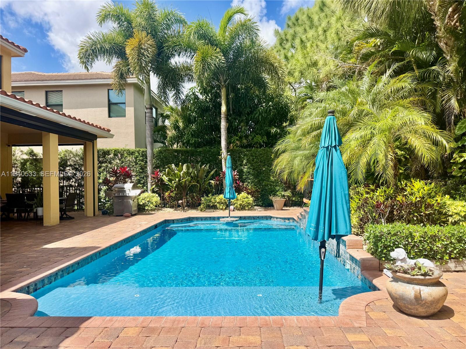 A rectangular swimming pool with a turquoise umbrella sits on a brick patio — 12097 Boca Reserve Ln, Boca Raton FL 33428, BOCA RATON, FL