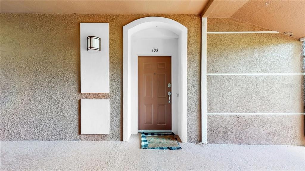 A brown front door with the number 103 is set within a stucco exterior wall — 8304 PORTOFINO DRIVE UNIT 103, DAVENPORT, FL