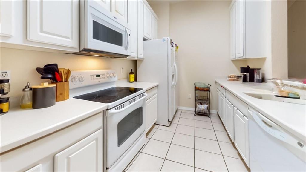 A galley-style kitchen features white cabinets, white appliances, and light-colored tile flooring — 8304 PORTOFINO DRIVE UNIT 103, DAVENPORT, FL