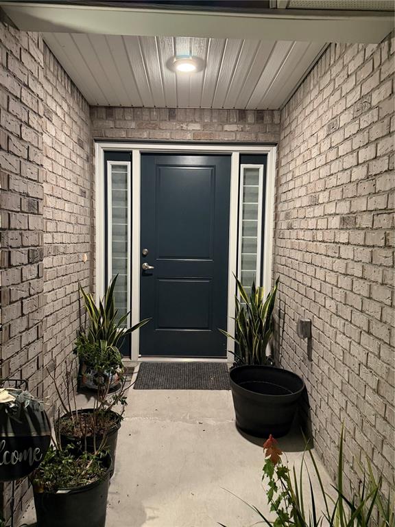 A dark blue front door with side windows is framed by brick walls and potted plants — 93 ROYAL OAK DRIVE, PALM COAST, FL