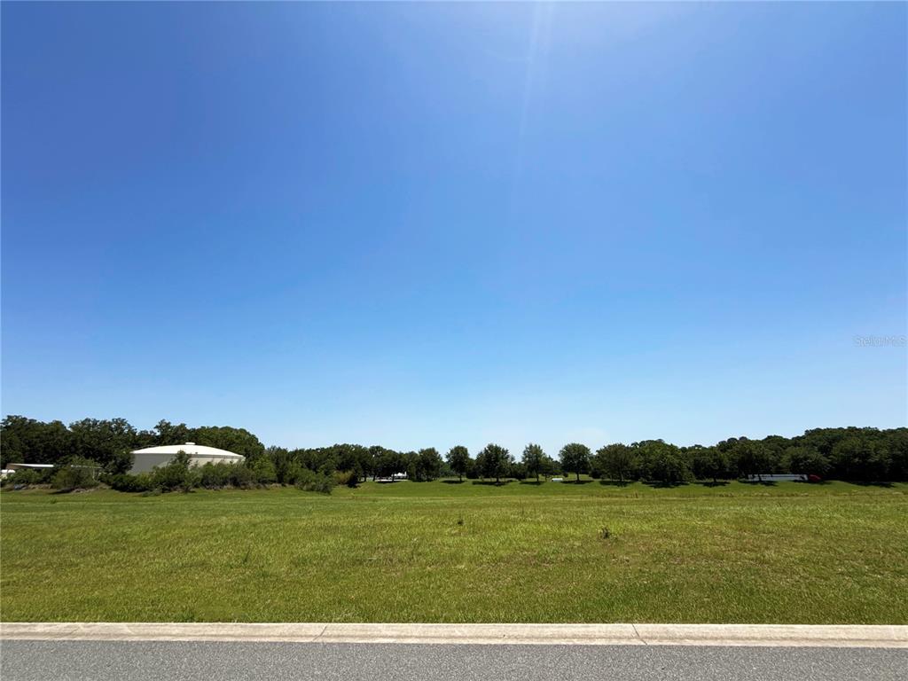 A wide, grassy vacant lot sits under a clear blue sky with distant trees — XX NW 17TH CIRCLE, OCALA, FL