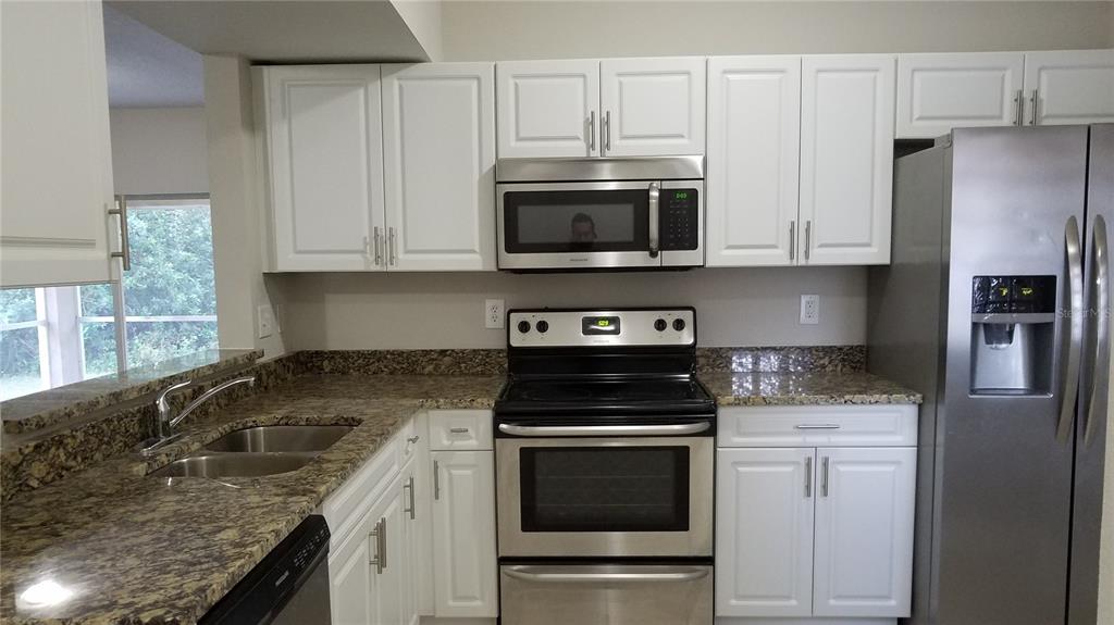 A kitchen features white cabinets, stainless steel appliances, and granite countertops — 6012 PORTSDALE PLACE UNIT 101, RIVERVIEW, FL